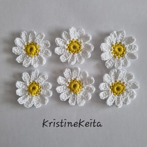 May include: Six individual crochet daisy appliques arranged in two rows of three. Each flower features white petals surrounding a bright yellow centre. The text KristineKeita is printed in a simple black font below the flowers on a plain background.