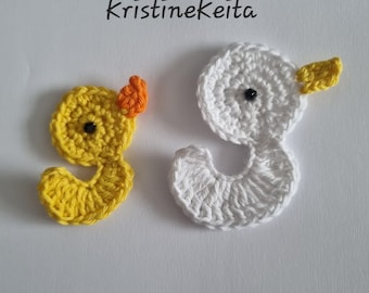 May include: Two crochet duck appliques, one yellow with an orange beak and one white with a yellow beak, each featuring a small black bead eye. The text KristineKeita is printed above the two crocheted figures on a plain white background.
