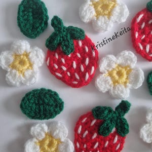 May include: A collection of crocheted appliques featuring red strawberries with white embroidered seeds and green leaves, white flowers with yellow centres, and solid green leaves. The text KristineKeita is visible in black script.