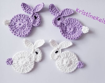 May include: Four crocheted bunny appliques in lavender and white. Each bunny has a round body, long ears, and a small pom-pom tail. The text "kristinekeita" is written in purple script.