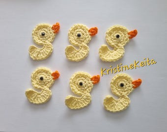 May include: Six crocheted yellow duck appliques with orange beaks and black eyes. The ducks are arranged in two rows of three.