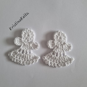 May include: Two white crochet angel ornaments featuring a circular head, small outstretched wings, and a flared skirt with an openwork stitch pattern. The text Kristinekeita is printed in black ink in the upper left corner of the image.