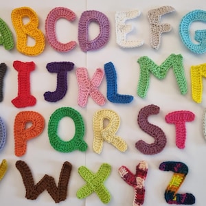 May include: A collection of colorful, crocheted alphabet letters. Each letter is a different color, including green, yellow, pink, and blue. The letters are arranged in rows, showcasing the entire alphabet. Ideal for educational crafts or personalized decor.