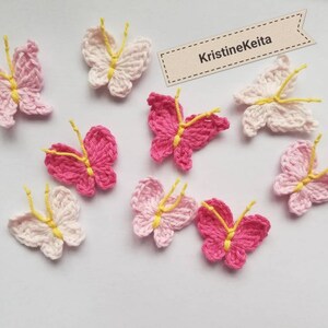 May include: A collection of handmade crochet butterflies in various shades of pink and white, with yellow accents. The butterflies are arranged on a light background. The image includes a tag with the text "KristineKeita".
