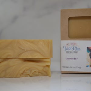 May include: Two bars of light brown goat milk soap with a swirl pattern, packaged in a brown box with a white label that reads "Irish Blue Goat Milk Soap", "Lavender", "Net Wt. 4.4 oz (124g)", and "Jetta".