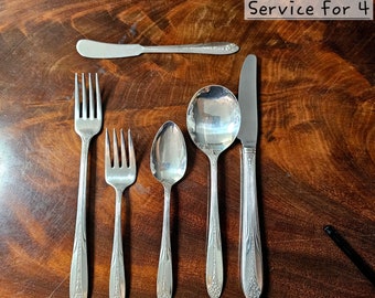 May include: Silverware set for four, including forks, spoons, a knife, and a butter knife. The utensils are arranged on a wooden surface. The text "Service For 4" is displayed in the upper right corner.