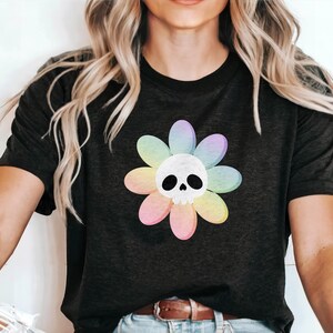Pode incluir: Uma camiseta preta com um gr&aacute;fico de flor arco-&iacute;ris com uma caveira branca no centro.