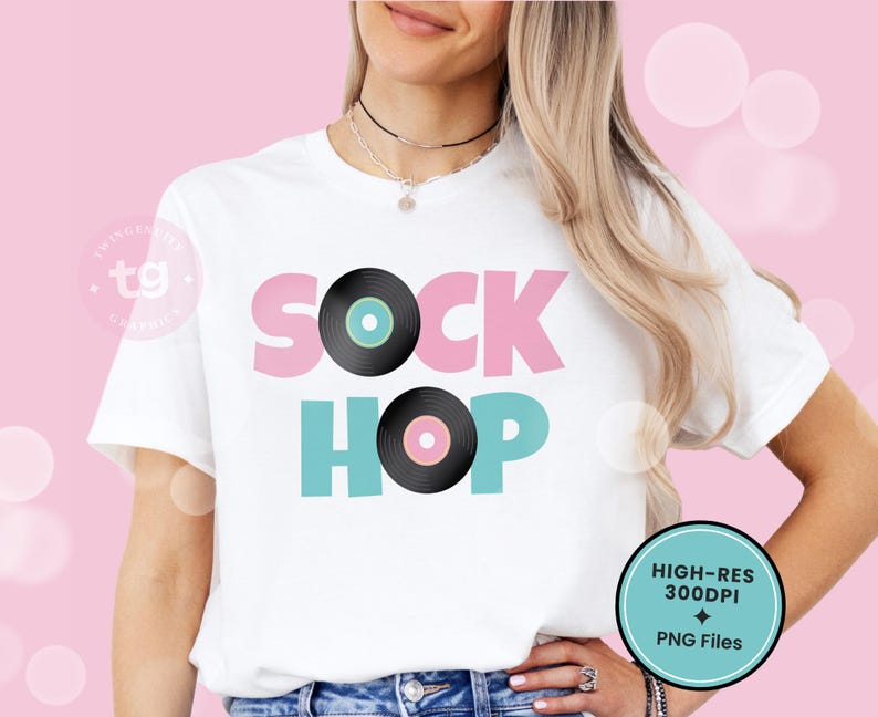 Puede incluir: Una camiseta blanca de manga corta con el texto SOCK HOP en letras de bloque rosas y turquesas. La letra O de SOCK est&aacute; sustituida por un disco de vinilo negro con el centro turquesa, y la O de HOP por un disco negro con el centro rosa.