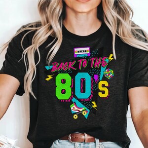 May include: Black t-shirt with a graphic design featuring the text "Back to the 80's" in neon colors with a cassette tape, roller skate, and geometric shapes.