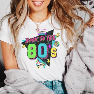 May include: A white t-shirt with a graphic design featuring a cassette tape, a rainbow-colored 80s font, and the text "Back to the 80s".