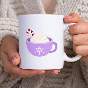 May include: White ceramic mug with a purple design of a mug of hot chocolate with whipped cream and a candy cane. The mug has a snowflake design.
