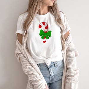 Puede incluir: Camiseta blanca con un bast&oacute;n de caramelo rojo y blanco con un lazo verde en la parte superior.