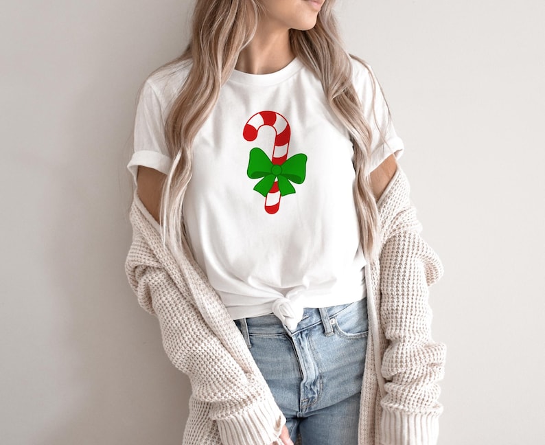 Puede incluir: Camiseta blanca con un bast&oacute;n de caramelo rojo y blanco con un lazo verde en la parte superior.