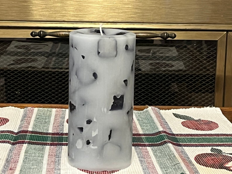May include: A white pillar candle with a black and white marbled design. The candle is sitting on a striped table runner.