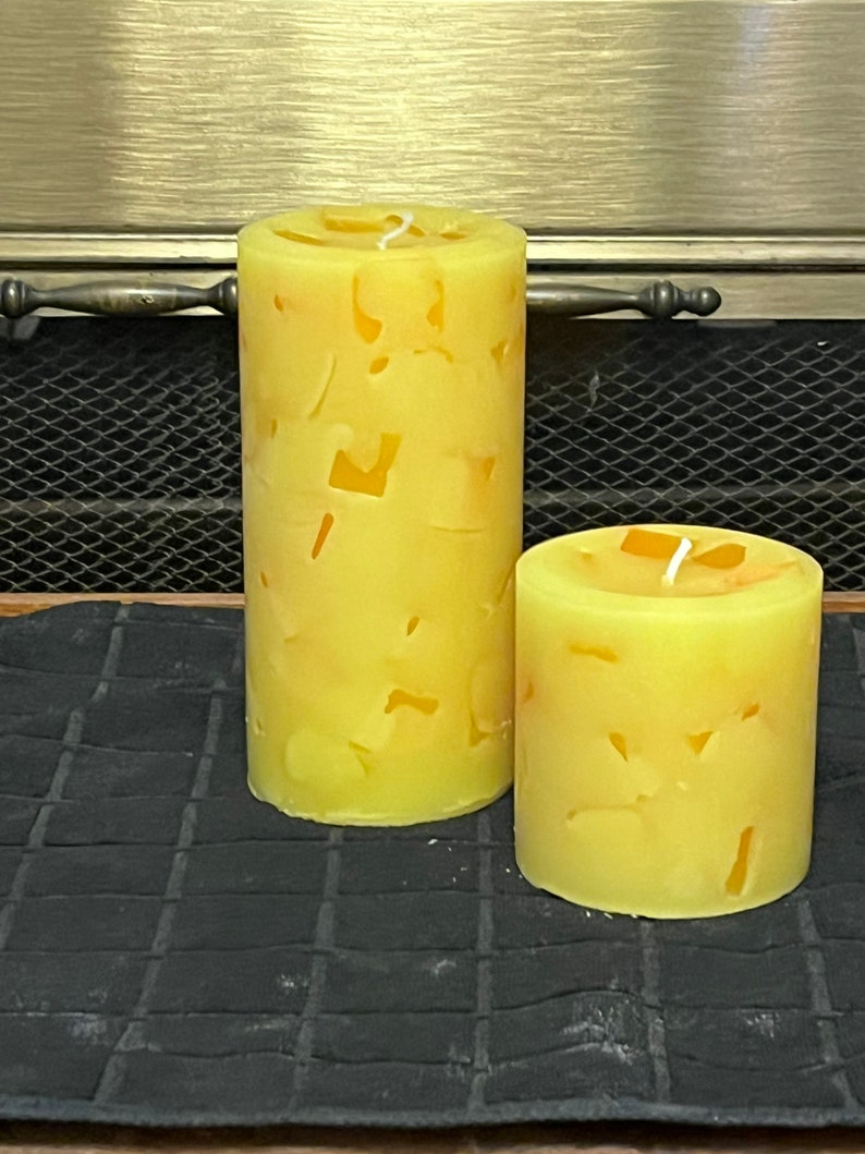 May include: Two yellow pillar candles with a textured surface. The candles are different sizes and are sitting on a black surface.