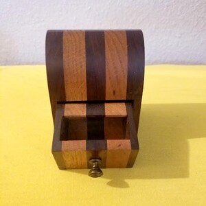 May include: A small wooden box with a drawer. The box is made of dark wood with light wood stripes. The drawer has a brass knob.