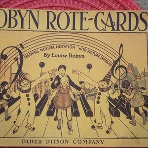May include: A vintage book cover with a yellow background and a colorful illustration of children playing on a piano keyboard. The title of the book is "Robyn Rote-Cards: Teaching Musical Notation with Picture Symbols by Louise Robyn".