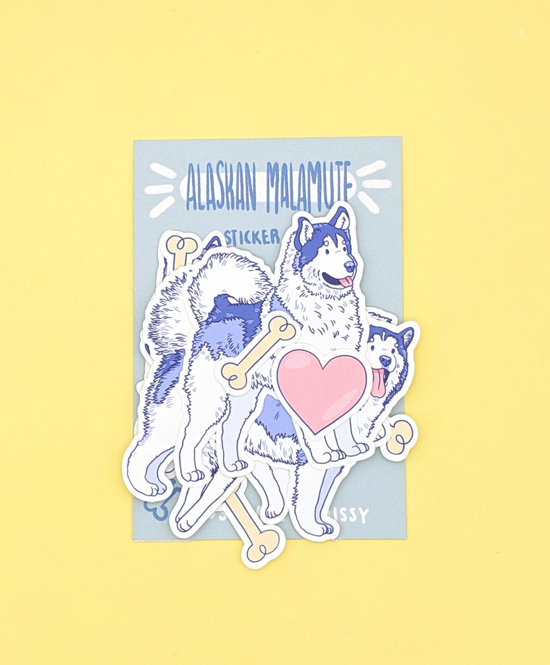Puede incluir: Una hoja de pegatinas con un perro esquimal de Alaska de dibujos animados con un coraz&oacute;n y huesos. La hoja de pegatinas est&aacute; sobre un fondo azul con el texto "Alaskan Malamute Sticker".