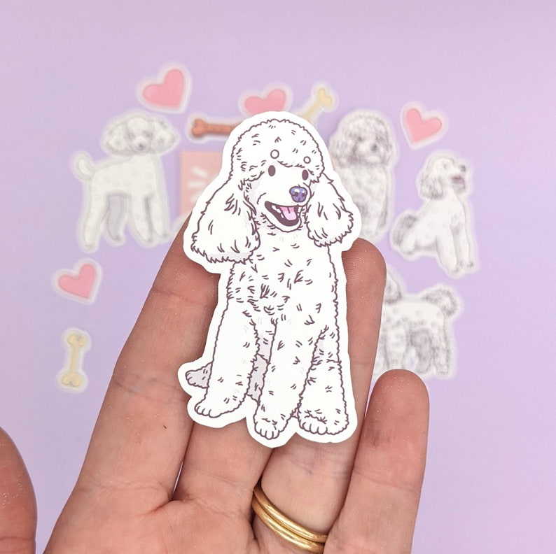Op de afbeelding: Een witte poedel sticker met een roze hart en bot stickers op een paarse achtergrond.