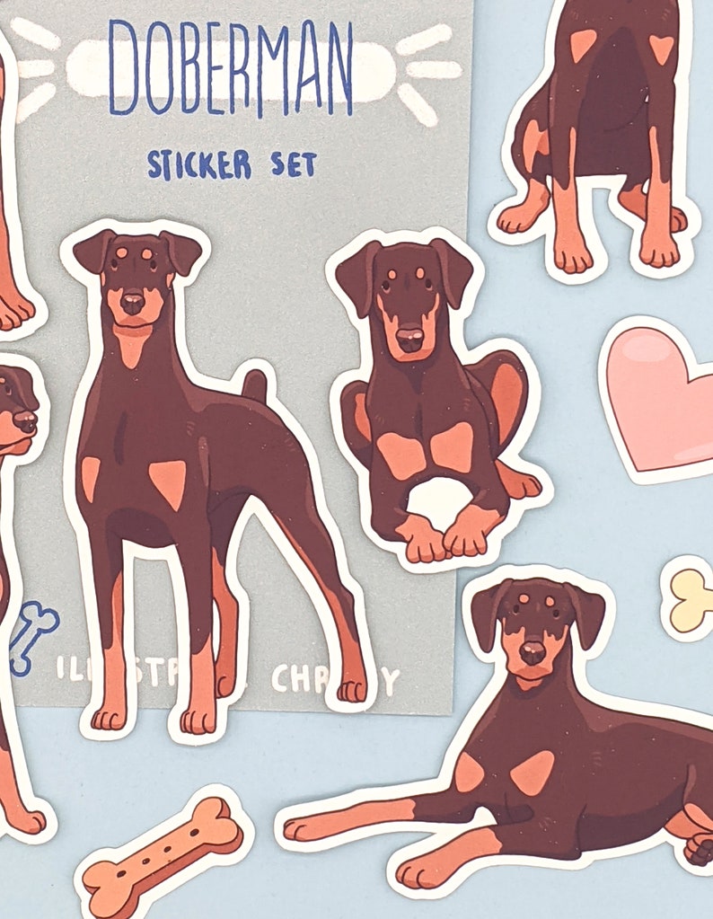 May include: A sticker set featuring illustrations of Doberman Pinschers in various poses. The stickers are on a light blue background with a bone and a heart. The text "Doberman Sticker Set" is on a gray background.