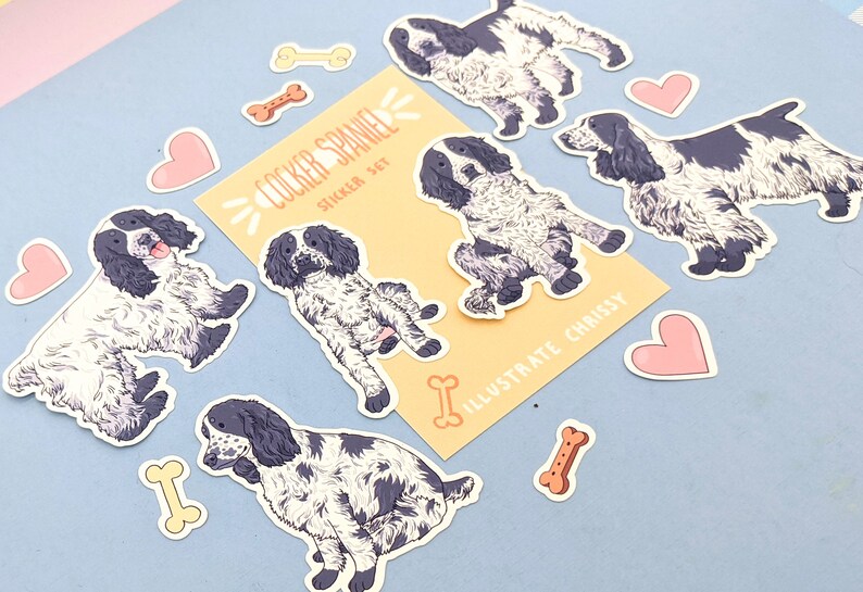 May include: A sticker set featuring Cocker Spaniel illustrations in black and white, along with pink hearts and bone-shaped stickers. The set includes a card with the text "COCKER SPANIEL STICKER SET" and "ILLUSTRATE CHRISSY".