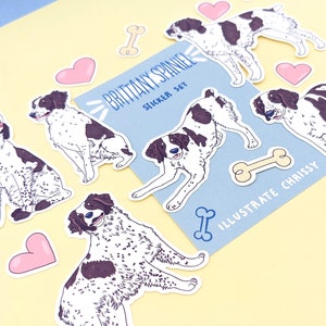 May include: A set of stickers featuring illustrations of Brittany Spaniel dogs in various poses. The stickers are on a light blue background with the text "Brittany Spaniel Sticker Set" and "Illustrate Chrissy". The stickers include hearts and bones.