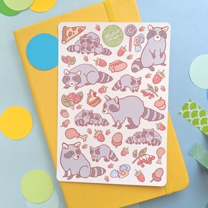 May include: A sticker sheet featuring cartoon raccoons, strawberries, pizza, and other food items. The raccoons are gray with striped tails. The text "Illustrate Chassy" is in a green circle. The sticker sheet is on a yellow notebook.