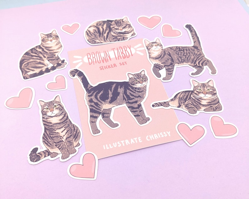 May include: A set of brown tabby cat stickers with pink hearts. The stickers feature different poses of the cat, including sitting, lying down, and walking. The stickers are on a pink background. The text "Brown Tabby Sticker Set" and "Illustrate Chrissy" are on the sticker sheet.