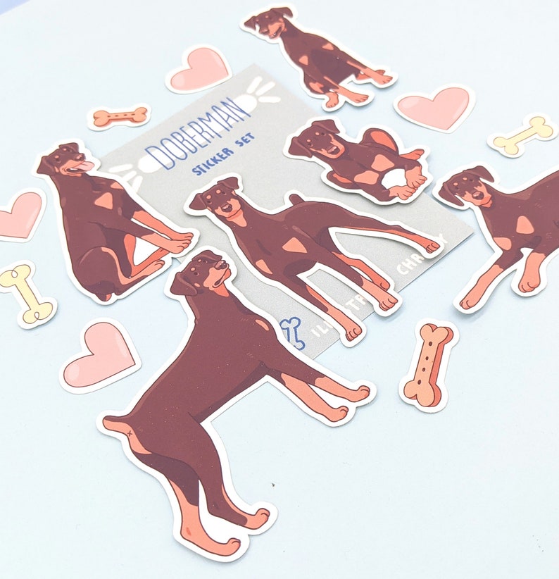 May include: A set of Doberman Pinscher dog stickers. The stickers are in various poses and feature a brown and black color scheme. The stickers are on a light blue background. The text "Doberman Sticker Set" is on one of the stickers.