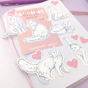 May include: A sticker set featuring illustrations of white cats in various poses, with pink heart stickers. The set includes a pink card with the text "WHITE CAT STICKER SET" and "ILLUSTRATE CHRISSY". The stickers are on a dotted notebook page.