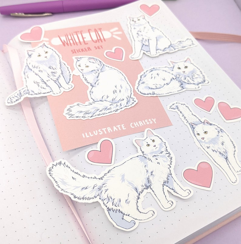 May include: A sticker set featuring illustrations of white cats in various poses, with pink heart stickers. The set includes a pink card with the text "WHITE CAT STICKER SET" and "ILLUSTRATE CHRISSY". The stickers are on a dotted notebook page.