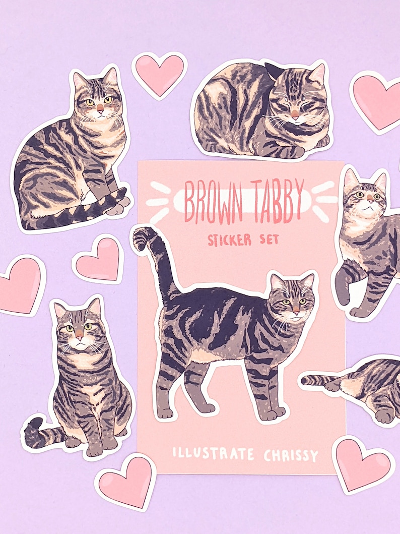 May include: A set of brown tabby cat stickers with pink hearts. The stickers feature different poses of the cat, including sitting, lying down, and standing. The sticker sheet includes the text "Brown Tabby Sticker Set" and "Illustrate Chrissy".
