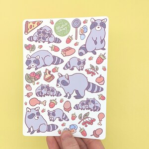May include: A sticker sheet featuring cartoon raccoons and various food items like pizza, strawberries, and a lollipop. The sheet includes the text "Illustrate Chrissy" in a green circular design. The raccoons are in various poses, with gray and white fur.