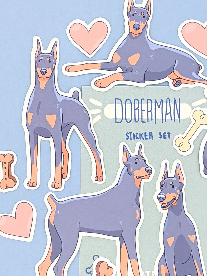 May include: A sticker set featuring Doberman Pinschers in various poses. The stickers are in a cartoon style with a light blue and pink color scheme. The set includes a bone, hearts, and the text "Doberman Sticker Set".