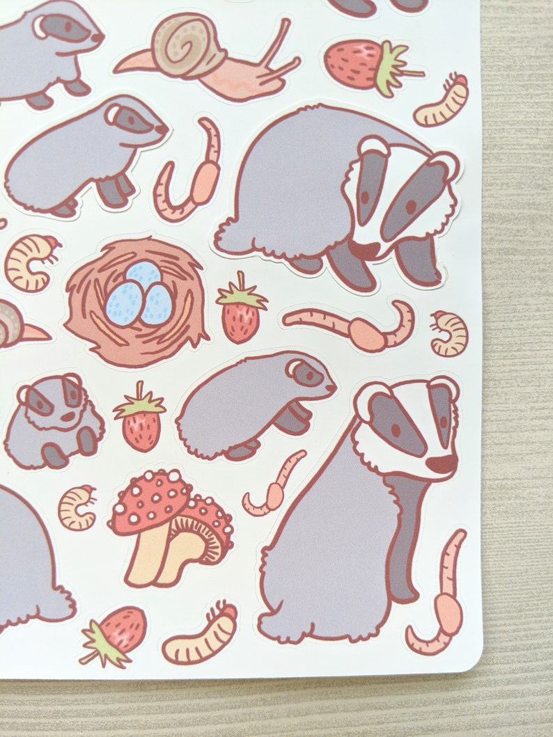 K&ouml;nnte beinhalten: Eine Bogen mit Aufklebern mit Illustrationen von Dachsen, Schnecken, Erdbeeren, Pilzen und W&uuml;rmern. Die Aufkleber sind in verschiedenen Farben, darunter rosa, rot, braun und gr&uuml;n.