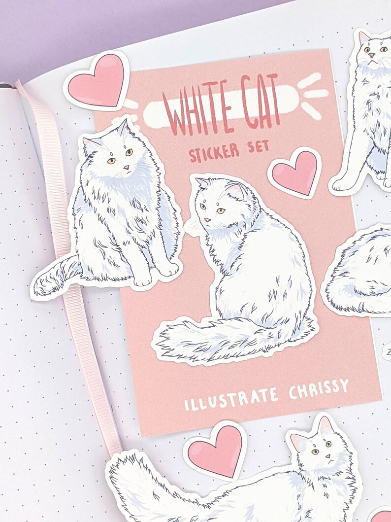 May include: A sticker set featuring illustrations of white cats with yellow eyes and pink heart stickers. The set includes a pink card with the text "WHITE CAT STICKER SET" and "ILLUSTRATE CHISSY". The stickers are placed on a dotted background.