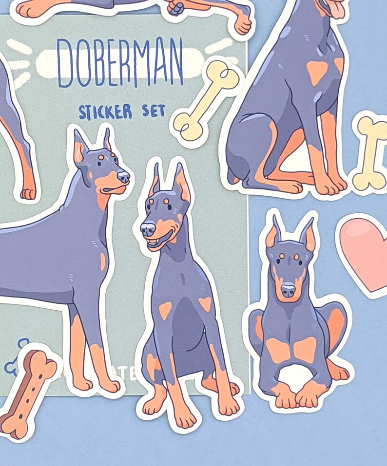 May include: A sticker set featuring illustrations of Doberman Pinschers in various poses. The stickers are on a light blue background with the text "Doberman Sticker Set" and a bone graphic.