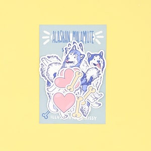 Puede incluir: Un conjunto de pegatinas con perros Alaskan Malamute con corazones y huesos. Las pegatinas est&aacute;n sobre un fondo azul claro con el texto "Alaskan Malamute" en azul.