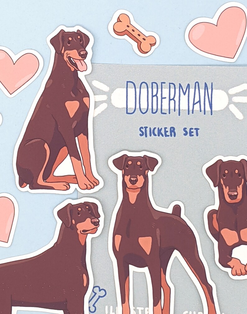 May include: A sticker set featuring Doberman Pinschers. The set includes four stickers of brown Dobermans in different poses, two pink hearts, a bone, and a title card that reads "Doberman Sticker Set".