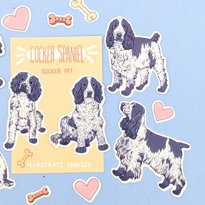May include: A sticker set featuring Cocker Spaniel illustrations in black and white, along with bone and heart-shaped stickers. The set includes the text "COCKER SPANIEL STICKER SET" and "ILLUSTRATE CHRISSY" on a yellow background.