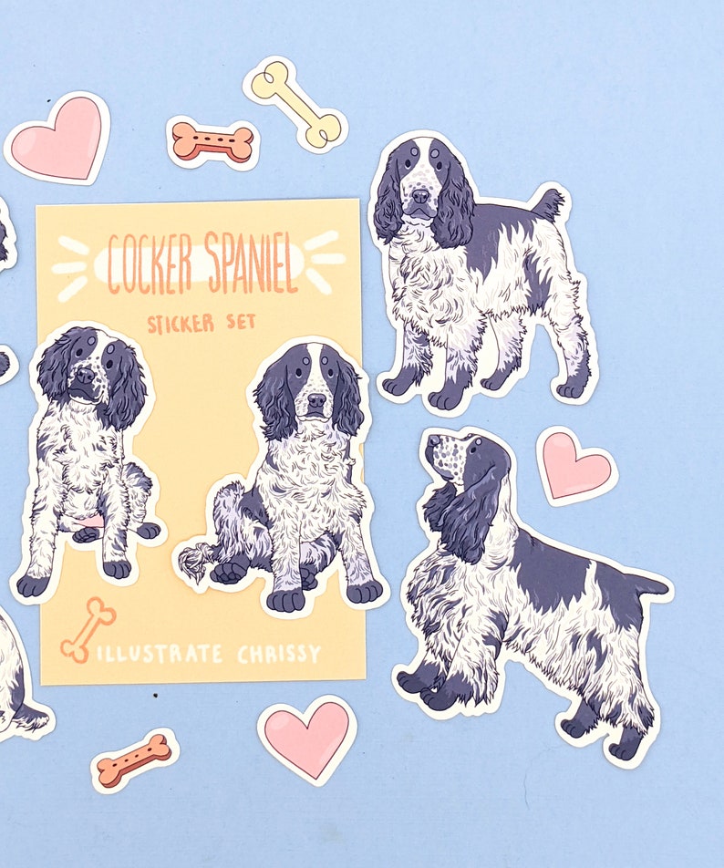 May include: A sticker set featuring Cocker Spaniel illustrations in black and white, along with bone and heart-shaped stickers. The set includes the text "COCKER SPANIEL STICKER SET" and "ILLUSTRATE CHRISSY" on a yellow background.