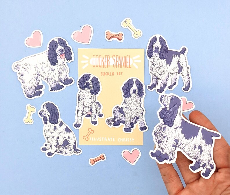 May include: A sticker set featuring Cocker Spaniel illustrations in various poses, with accents of pink hearts and bone shapes. The stickers have a white background with blue and white Cocker Spaniel designs. The text "Cocker Spaniel Sticker Set" is also included.
