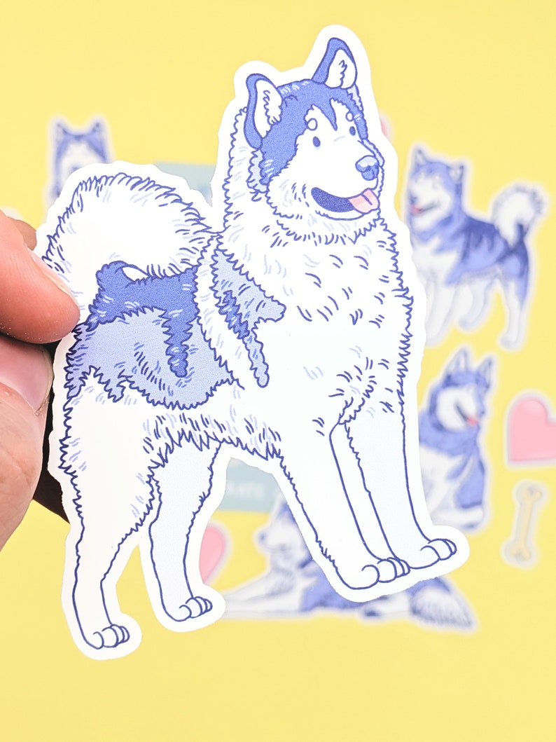 Puede incluir: Una pegatina azul y blanca de un perro esquimal de Alaska de dibujos animados con una cola esponjosa y la lengua fuera. La pegatina est&aacute; sobre un fondo amarillo.