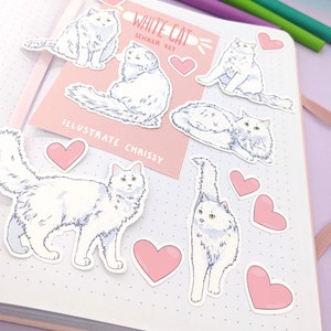May include: A collection of white cat stickers and pink heart stickers arranged on a notebook. The stickers feature illustrations of fluffy white cats in various poses. The text "WHITE CAT STICKER SET" and "ILLUSTRATE CHRISSY" are visible.