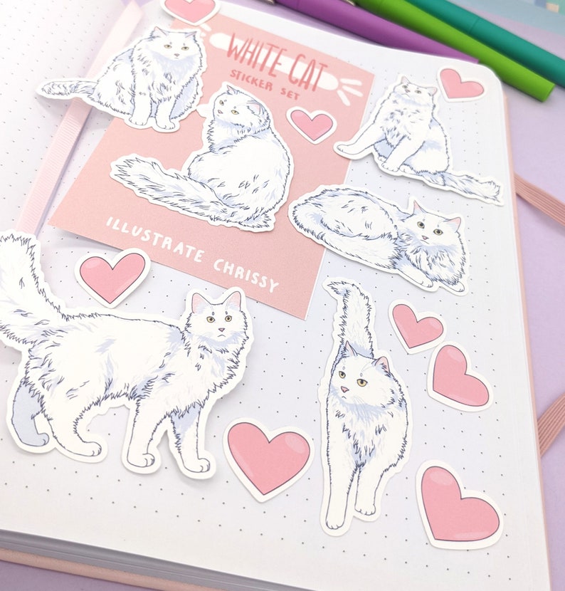 May include: A collection of white cat stickers and pink heart stickers arranged on a notebook. The stickers feature illustrations of fluffy white cats in various poses. The text "WHITE CAT STICKER SET" and "ILLUSTRATE CHRISSY" are visible.