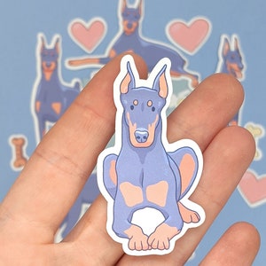 May include: A sticker featuring a cartoon illustration of a blue and pink Doberman Pinscher dog. The dog is sitting with its legs crossed and has a friendly expression.