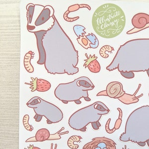 K&ouml;nnte beinhalten: Eine Bogen mit Aufklebern mit Illustrationen von Dachsen, Schnecken, Erdbeeren, W&uuml;rmern und Eiern. Die Aufkleber sind im Cartoon-Stil mit Pastellfarben gehalten. Der Text "Illustrate Chrissy" ist in Kursivschrift auf einem gr&uuml;nen Kreis geschrieben.