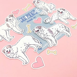 May include: A set of Great Pyrenees dog stickers with hearts and bones. The stickers are white with black markings and have a cartoon style. The stickers are on a pink background.
