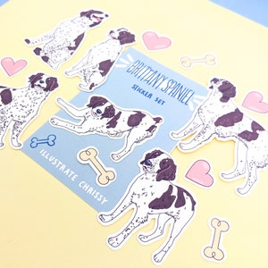 May include: A set of stickers featuring illustrations of Brittany Spaniels in various poses. The stickers are on a light blue background with the text "Brittany Spaniel Sticker Set" and "Illustrate Chrissy".