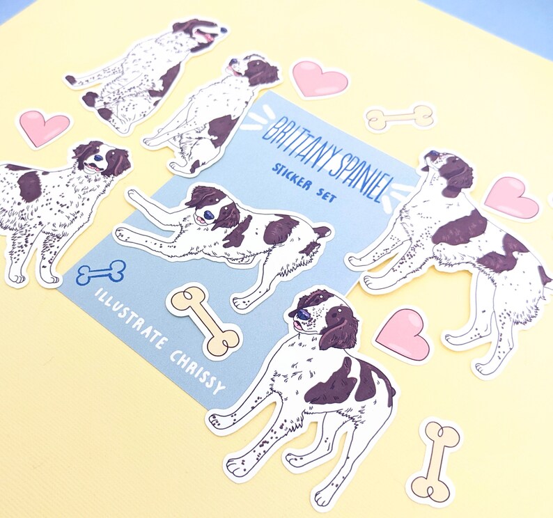 May include: A set of stickers featuring illustrations of Brittany Spaniels in various poses. The stickers are on a light blue background with the text "Brittany Spaniel Sticker Set" and "Illustrate Chrissy".
